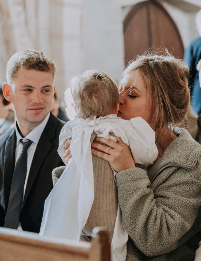 Eine Mutter hält ihr Kind während des Taufgottesdienstes liebevoll im Arm. Eine ruhige, emotionale Momentaufnahme in der Kirche.